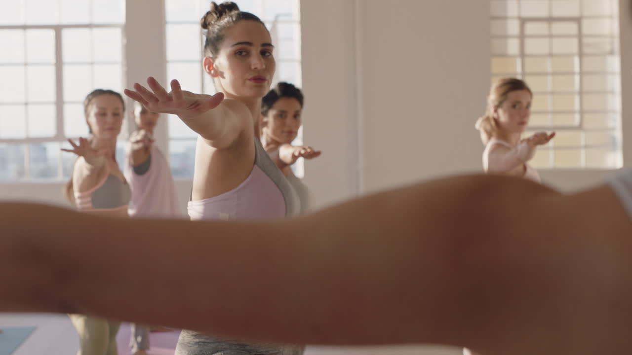 istruttore di lezione di yoga che insegna posa del guerriero a un bellissimo gruppo di donne che godono di uno stile di vita sano che si esercita nella sala fitness all'alba