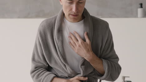 suffering man in pajamas and robe having a chest pain and touching his heart area in the morning at home 1