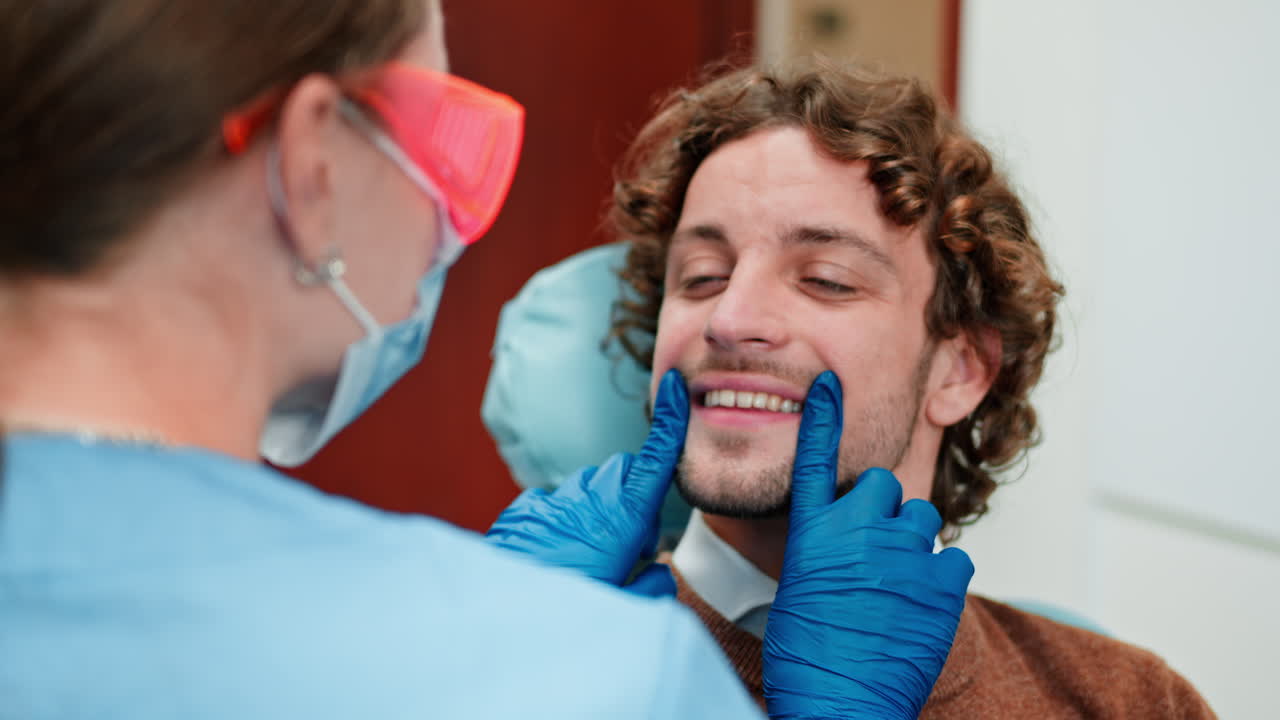 Un dentista con mascarilla de protección, gafas y guantes revisando los dientes de un paciente en una consulta dental.