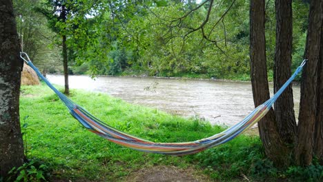 Tiro-Inclinado-Hacia-Arriba-De-Una-Hamaca-Frente-A-Un-Río-Grande-Y-Agradable-Rodeado-De-Un-Bosque-Profundo