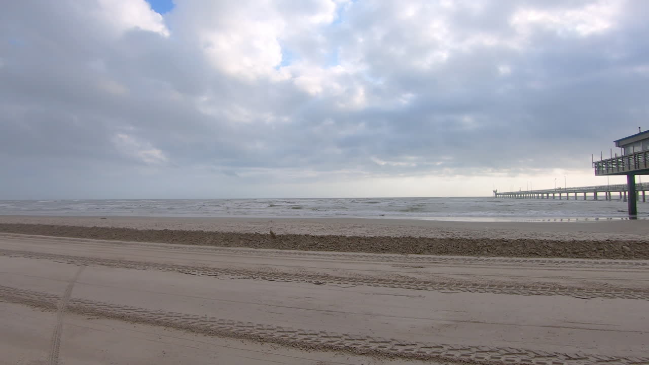 POV of a slowly driving vehicle on the beach past a fishing pier on North Padre Island National near Corpus Christi Texas USA as storm approaches