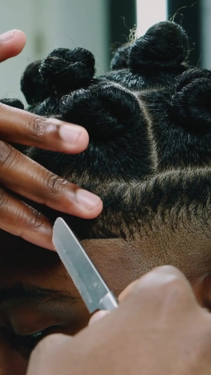 Vertical video: Hands lifting man's hair letting barber edging line at shop with razor, bantu knots