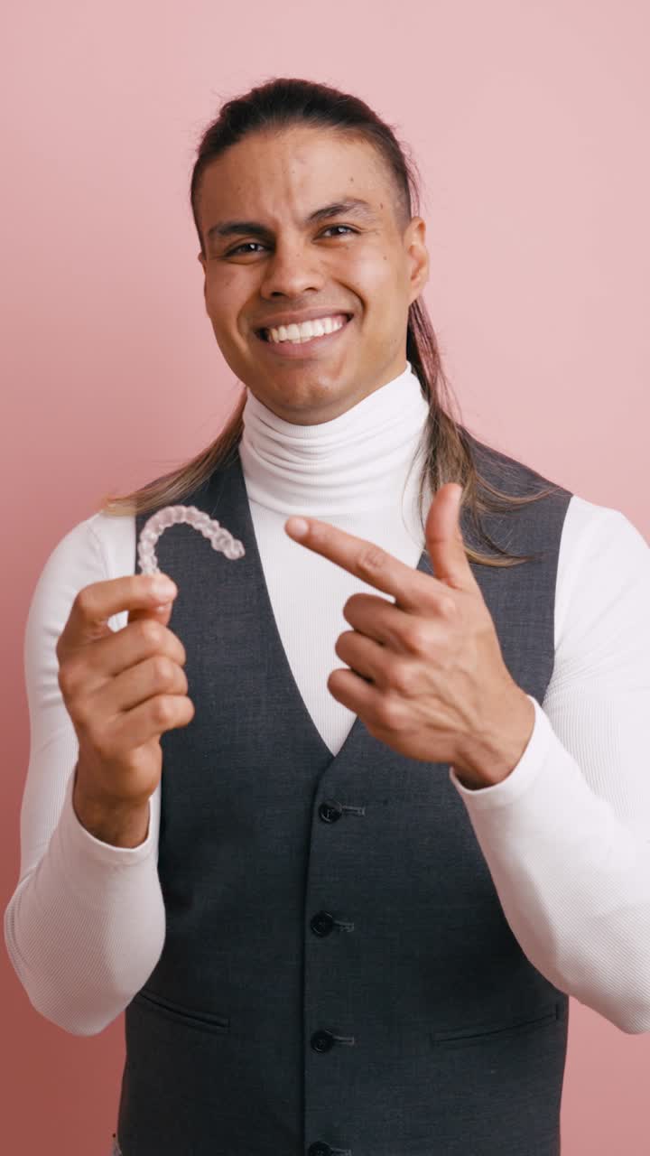 Smiling Man Holding and Pointing to a Clear Dental Aligner