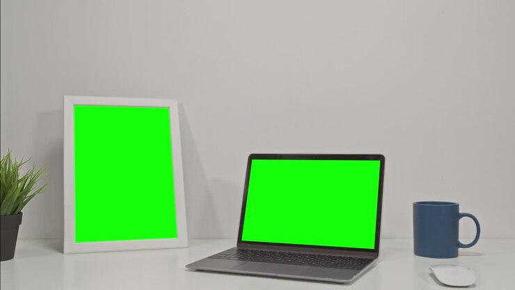 Two elecronic devices: laptop computer and tablet with green screen on a white office desk. Chroma key