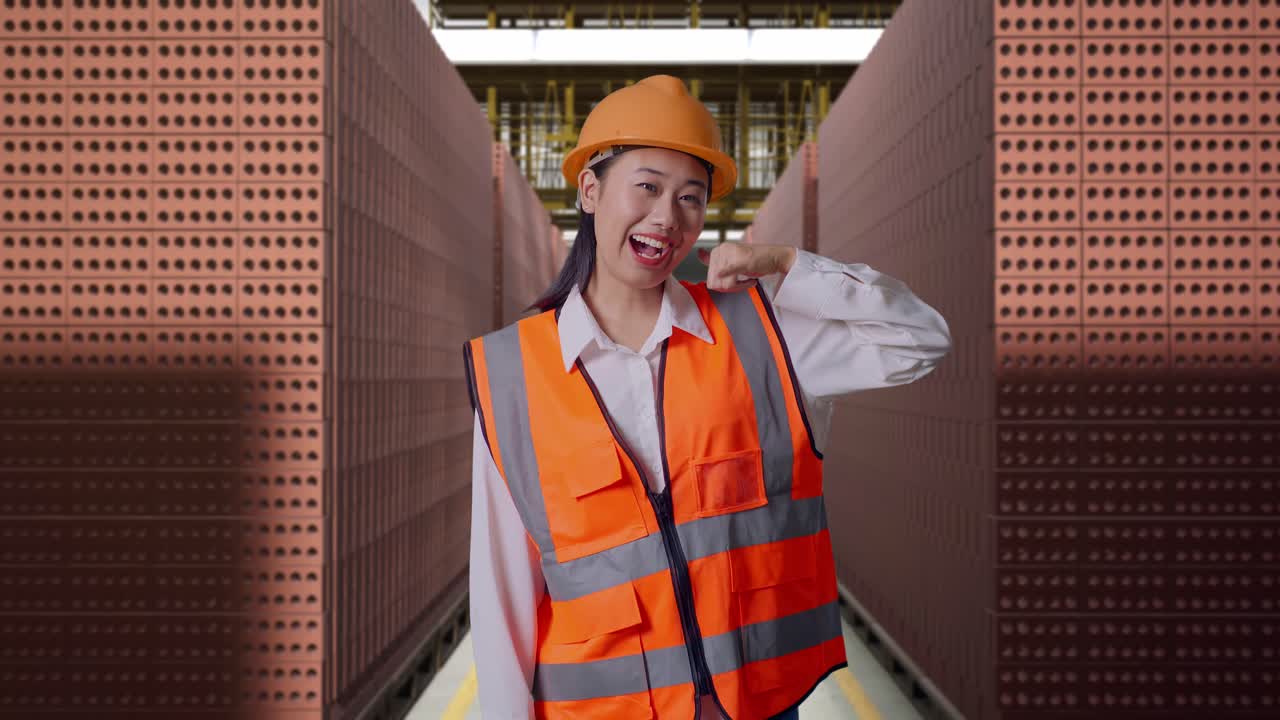 Asian Female Engineer With Safety Helmet Smiling To Camera And Making Call Me Gesture While Standing With Red Brick Packed in Stacks Are Stored