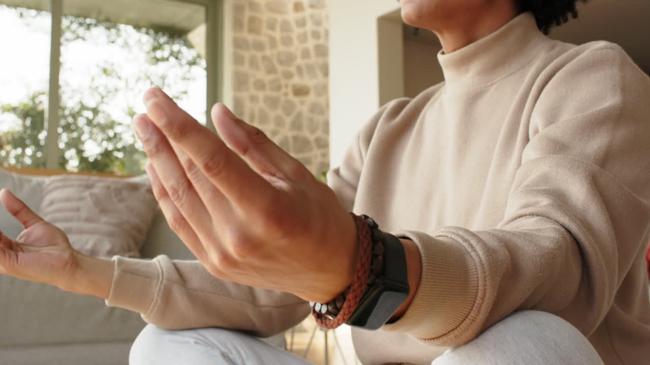 Uomo adulto asiatico che giunge le mani in preghiera e poi le abbassa in un mudra meditando accanto al divano