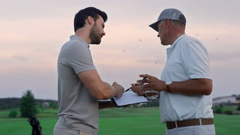 Active-sportsmen-discuss-golf-on-sunset-course.-Two-golfers-talk-at-country-club