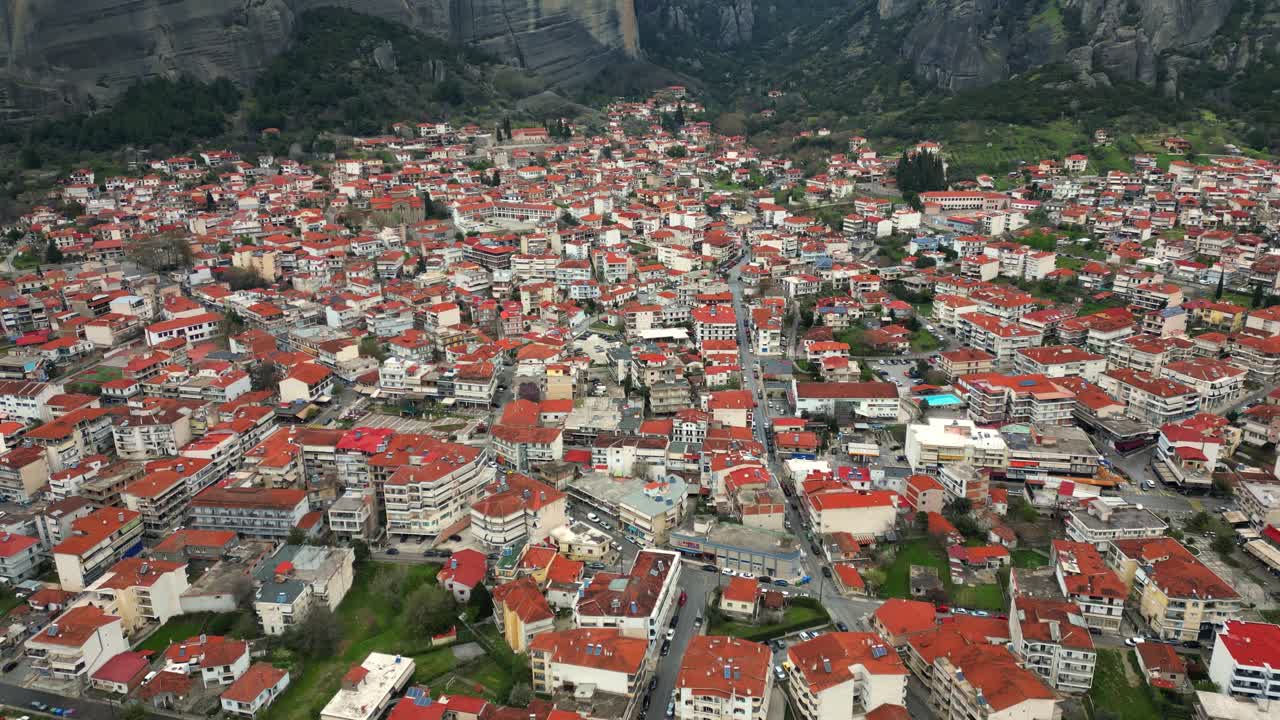 Aerial establishing tilt up across of Kalambaka town rooftops and streets with surrounding greenery, backdrop background