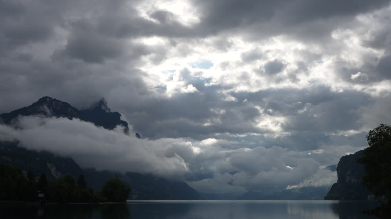 Overcast Sky with Clouds Breaking Over Majestic Mountains and Calm Lake