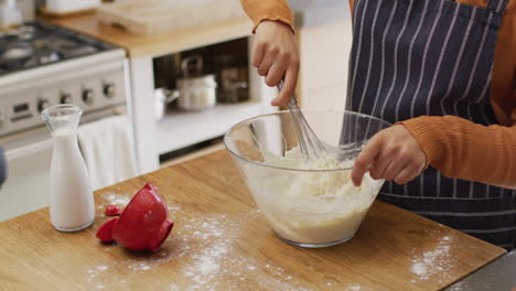 Video-of-midsection-of-biracial-woman-baking-in-kitchen-at-home,-mixing-cake-batter-in-mixing-bowl