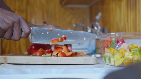 una toma estática en cámara lenta de un hombre negro en la cocina, cortando pimientos rojos cerca de un fregadero