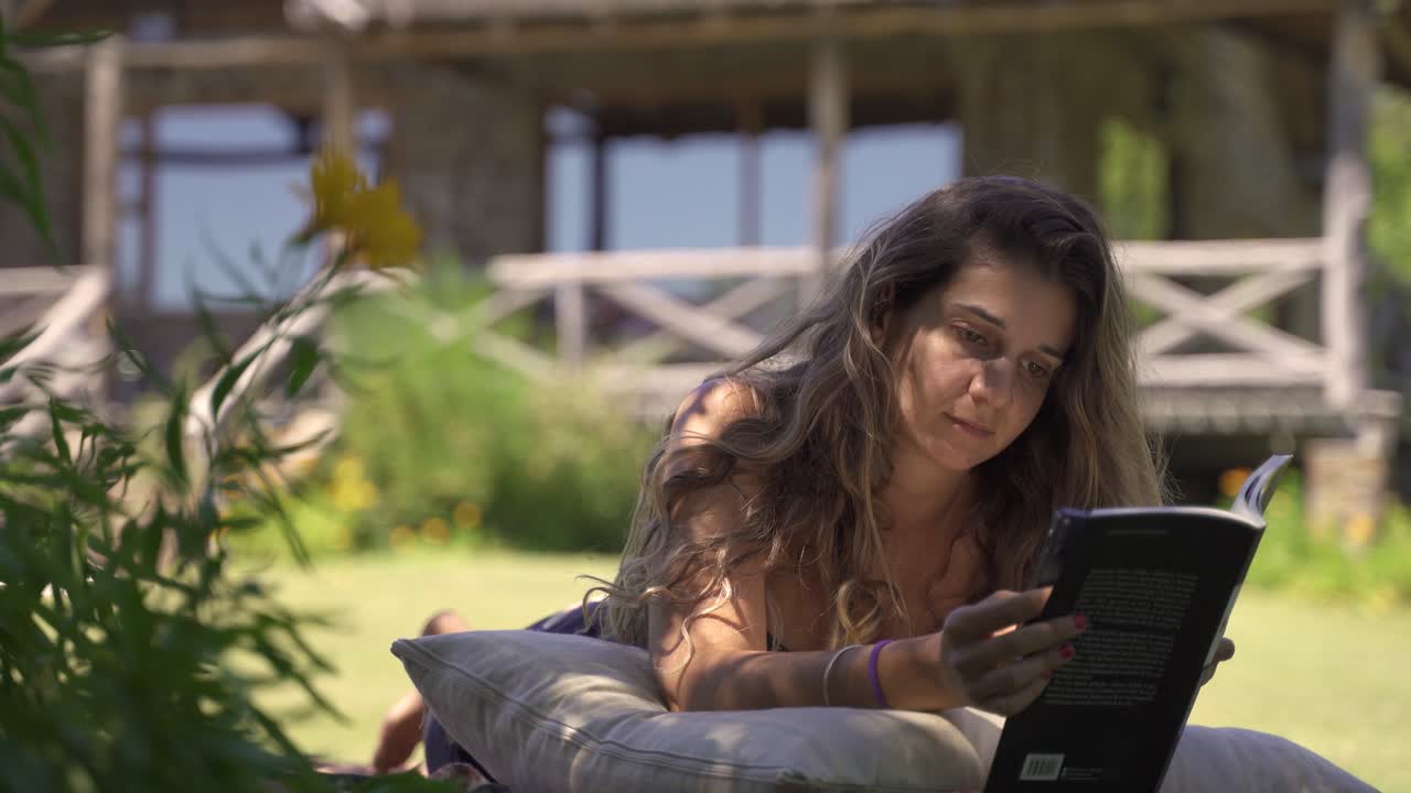 4.000 jóvenes mujeres latinas leyendo un libro serio al aire libre en el césped con un fondo de vegetación y casa