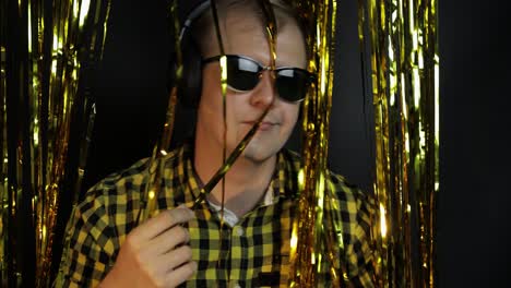 portrait of caucasian man dancing on black background. gold shining foil strips. party, music, disco