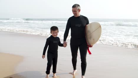 happy father and son in wetsuits walking on beach