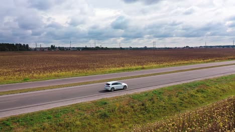 beautiful white car driving on the road on rural scenery background. drone view of the side of a car moving slowly on highway among nature.