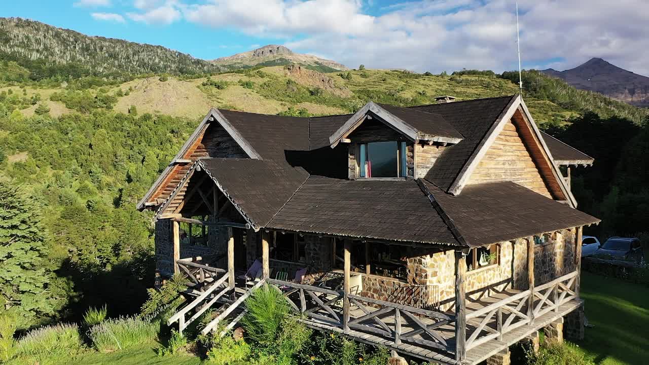 frente a una casa de piedra y madera de ensueño en las montañas al atardecer en movimiento vertical lento