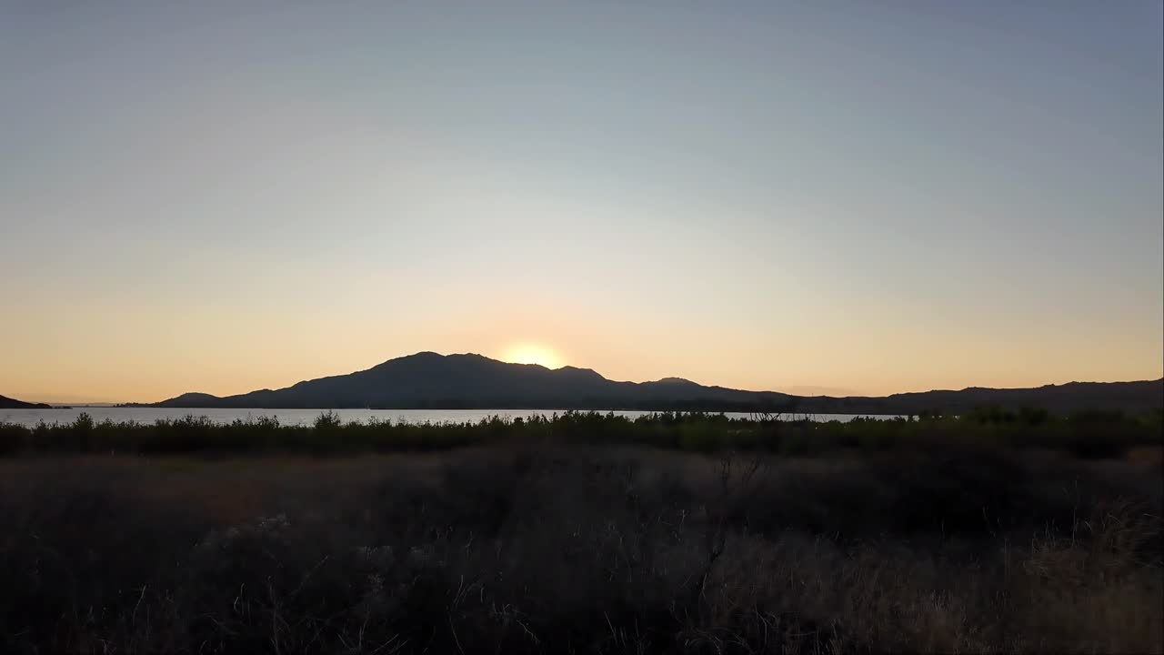 View of the sunset with the lake horizon and the mountain in the back. Lots of brown and green