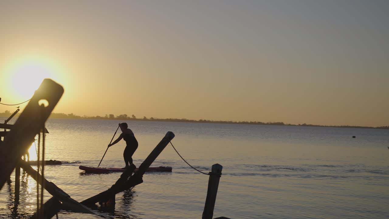 Silhuetter af to personer der paddleboarder på roligt vand ved solnedgang