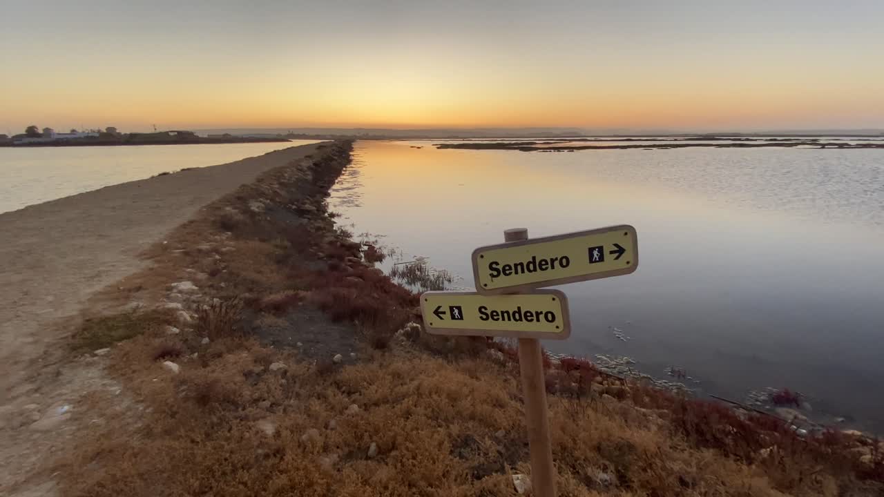Slow tilt up to a sunset in the marshes of Cadiz with trekking footpaths.