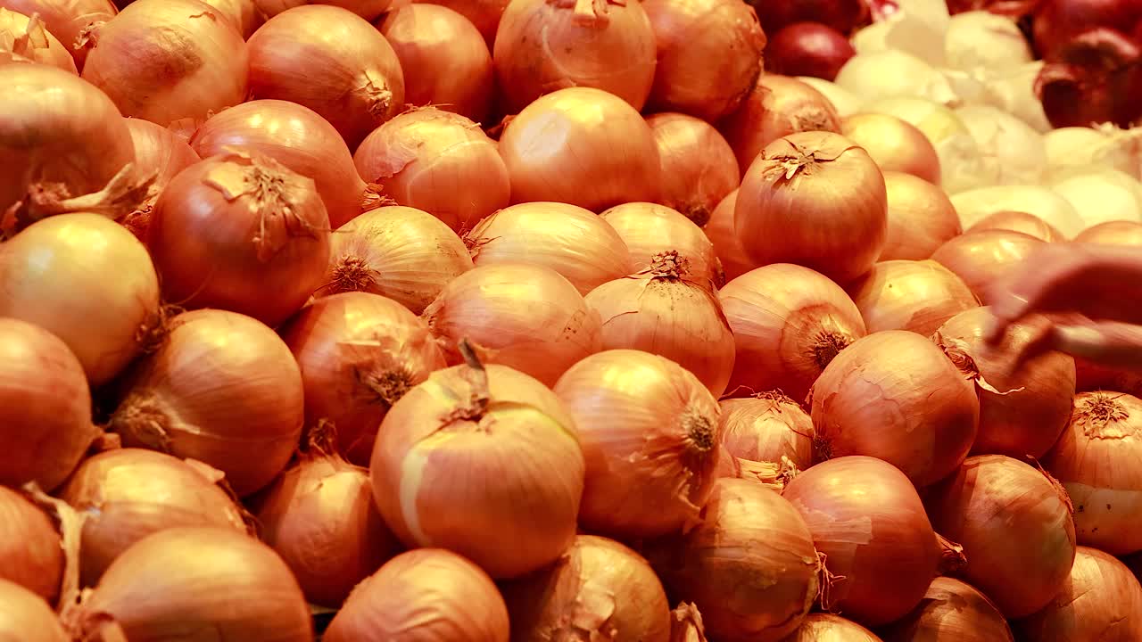 A hand reaches for yellow onions in a well-lit supermarket setting, highlighting fresh produce selection in Gold Coast, Australia