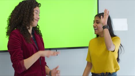 two businesswomen presenting to colleagues with green screen and high fiving