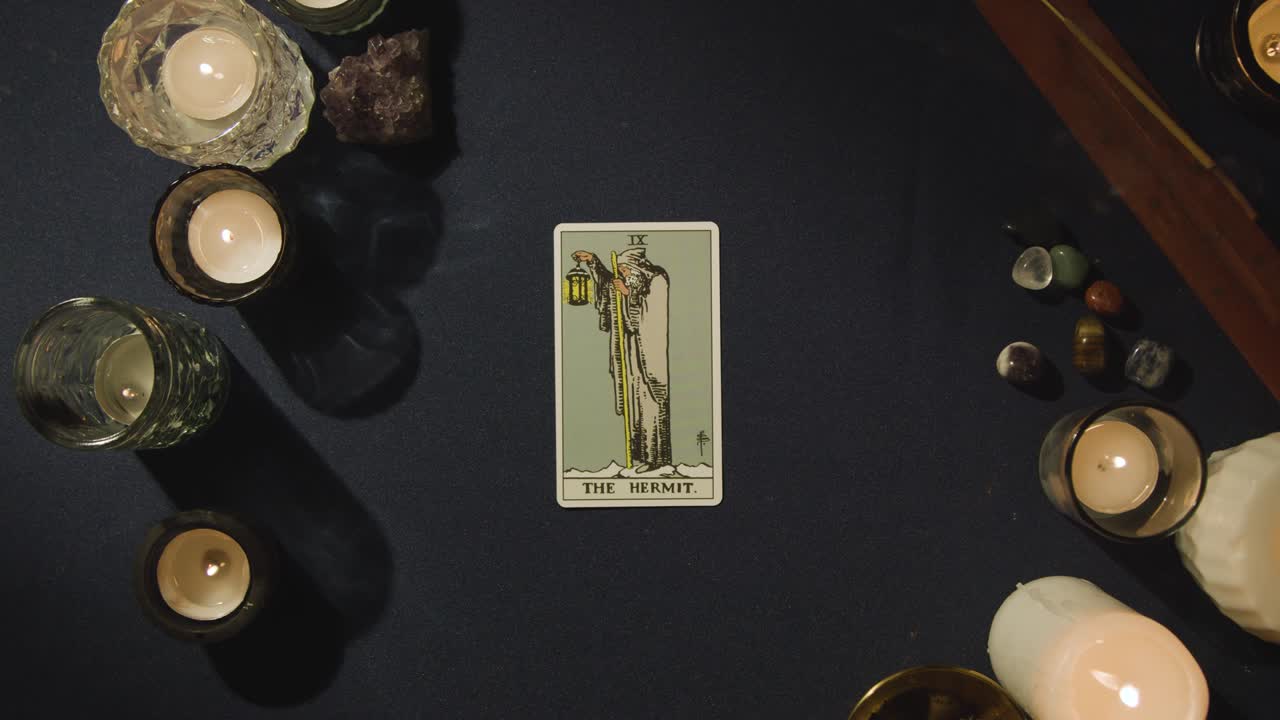 toma aérea de una persona que da lectura de cartas del tarot colocando las cartas del ermitaño, el rey de las espadas y el hombre ahorcado en la mesa