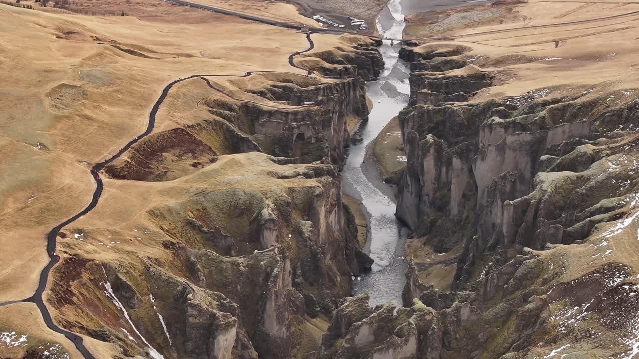 Aerial view of Fjaðrárgljúfur Canyon in Iceland, with steep cliffs and a meandering river cutting through the rugged golden landscape under soft daylight.
