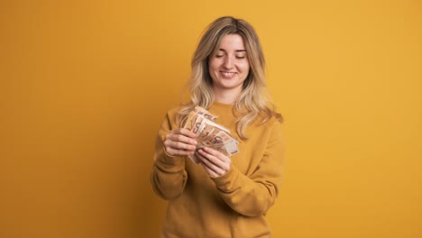 woman displaying cash in excitement over earnings from investment on yellow background