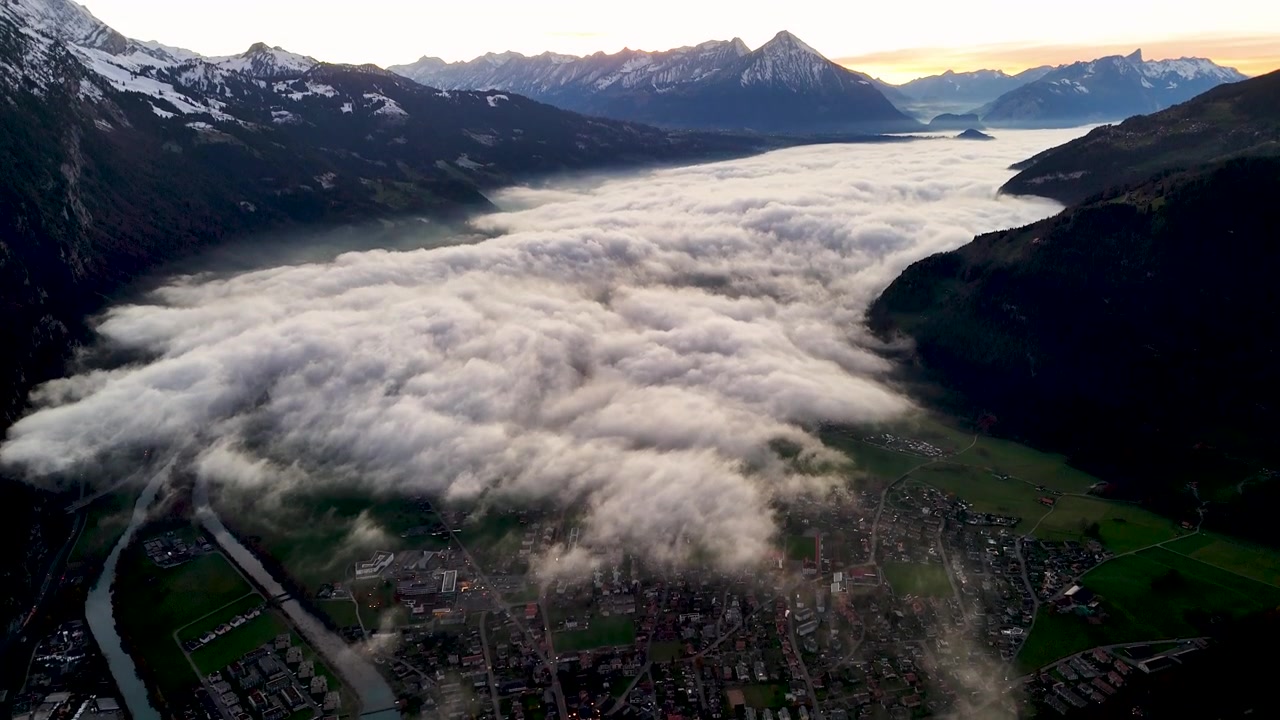 Luftfoto av Interlaken, Thunsjøen dekket av skyer, og de sveitsiske Alpene ved solnedgang