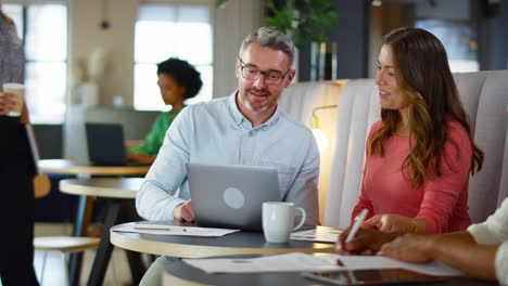 mature businesswoman and businessman working on laptop in informal seating area of modern office