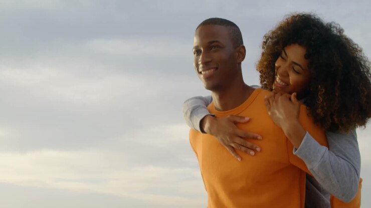 Ripresa dal basso di un uomo afroamericano che porta in spalla una donna sulla spiaggia 4k
