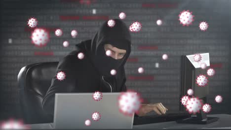 animación de las células macro covid19 sobre un hombre que lleva una balaclava, usando una computadora portátil