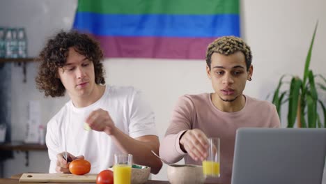 beautiful couple gay on the kitchen together preparing breakfast, watching news on laptop