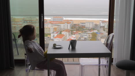 child having breakfast and watching cartoons in the apartment with ocean view