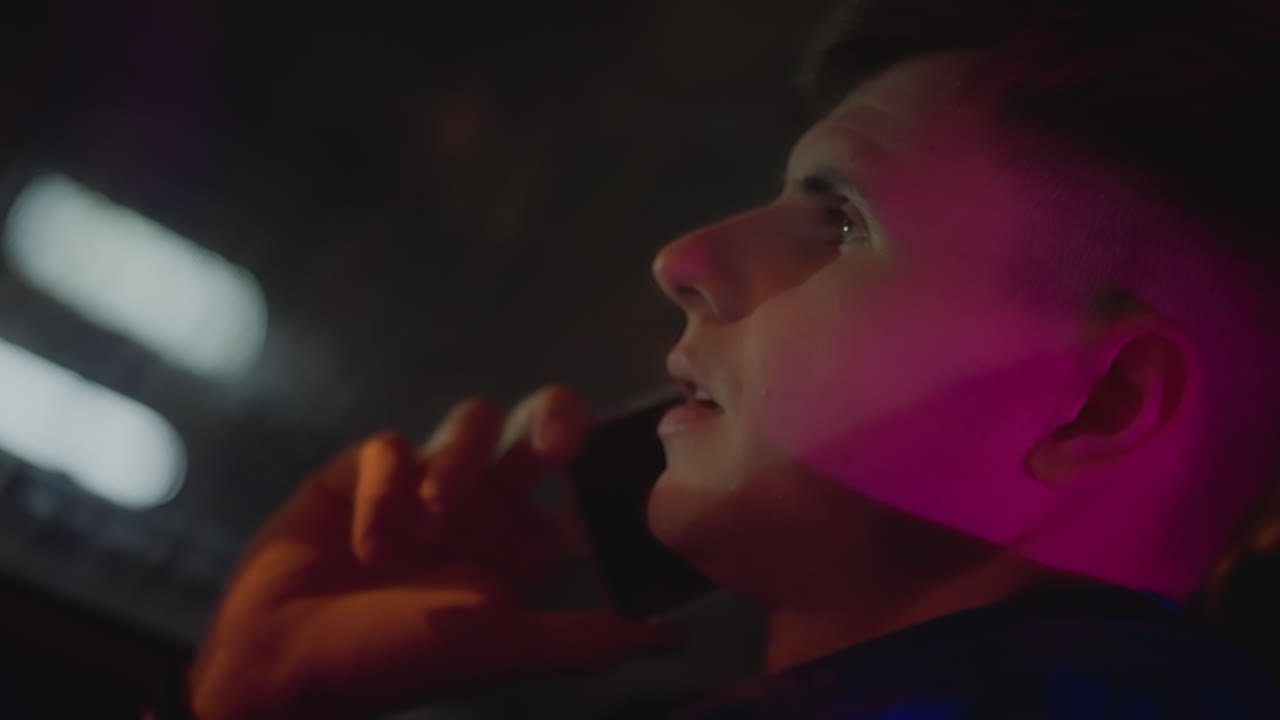 Man converses amid luminous reflections, Individual engaged in dialogue within colorful car surroundings, Person inside car speaks while vibrant neon reflections illuminate interior atmosphere
