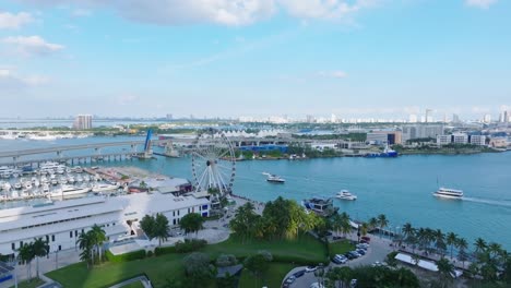 aerial view showing cruising boats at miami bayside with harbor and ferris wheel during sunny day with blue sky