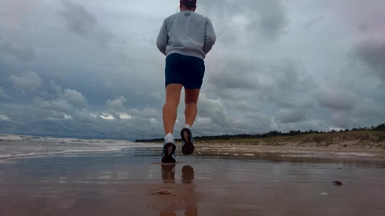 Mies juoksee rannalla aamulla. Tuulinen aamu, aaltoileva meri, sininen vesi, pilvinen, myrskyn edellä. Mies on hyvässä kunnossa