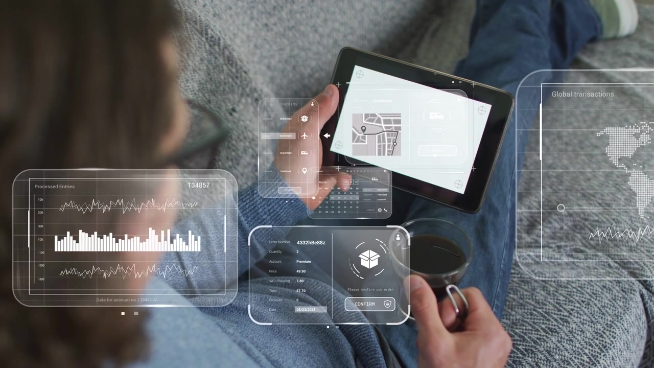 Uomo che tocca un tablet sul divano con una tazza, con grafici tecnologici, mappe, calendari e forme d'onda che si dispongono sopra il grembo.
