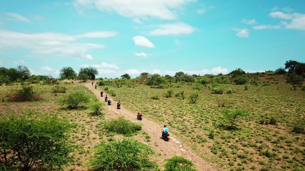 Un gruppo di motociclisti che guida su una strada sterrata attraverso i cespugli nel Parco Nazionale del Kenya, Africa Orientale
