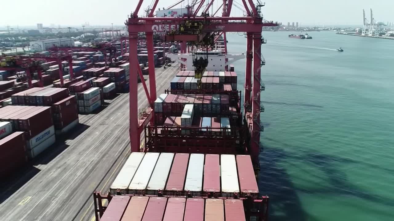 A container ship unloads goods at a bustling port. Cranes maneuver containers on the dock, highlighting the significance of marine logistics. Activity occurs under clear skies.