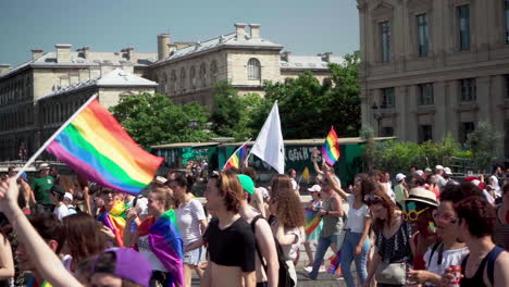 the marching crowd at the pride parade  in paris 2019. some of them are holding rainbow flags and a big white flag with a dark head is in the center of the frame.video is slowed down from 120 to 30.