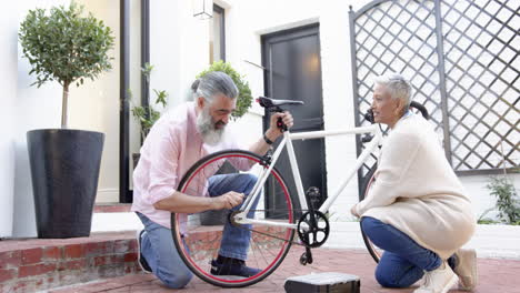 repairing bicycle, senior couple working together in front of house