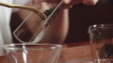 Asian-woman-puts-green-tea-leaves-from-glass-tray-into-Chinese-gaiwan-bowl-on-traditional-wooden-tea-table