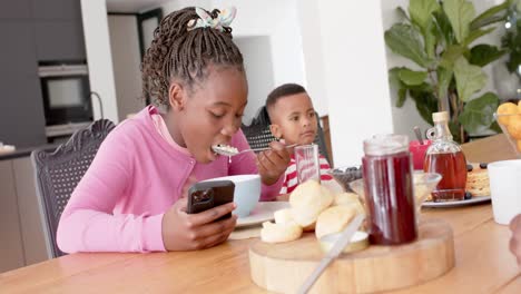 African-american-girl-eating-and-using-smattphone-in-kitchen,-slow-motion