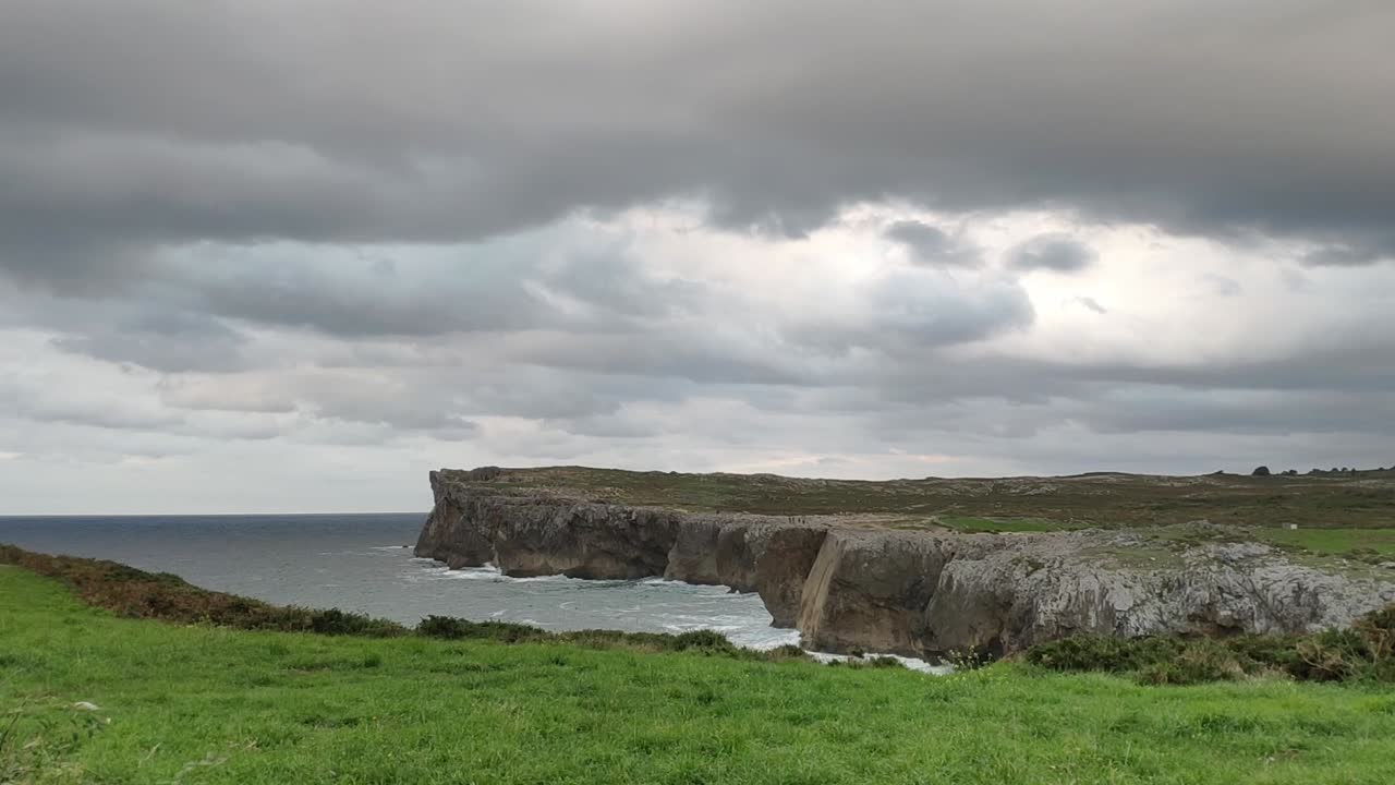 Cliffs at Guadamia in Asturias under moody skies, waves crash against rugged rocks