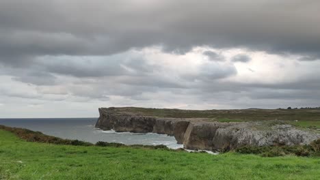 cliffs at guadamia in asturias under moody skies, waves crash against rugged rocks