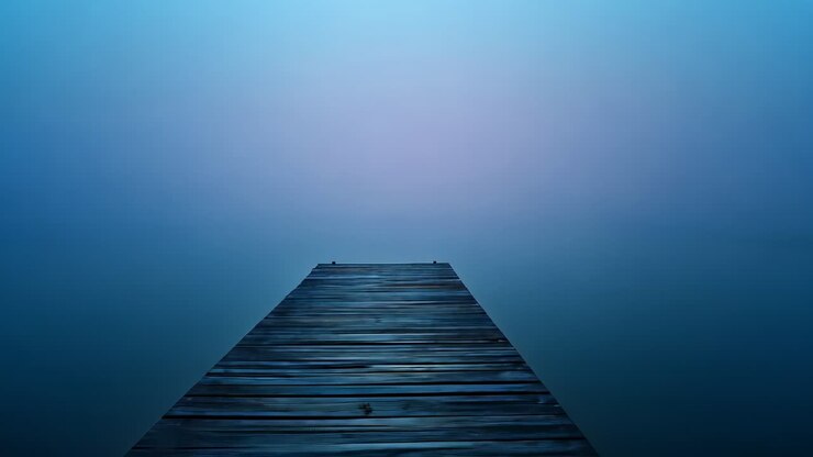 Extending wooden pier stretching into foggy lake, fog shifting and water surface gently shimmering