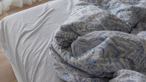 cama desordenada con ropa de cama con patrones azules y blancos