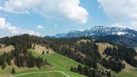 Glatte-Luftaufnahme-Der-Berglandschaft-Im-Entlebuch,-Schweiz,-Frühlingszeit-Mit-Pinien-Und-Schneebedeckten-Bergen-Bewölkt