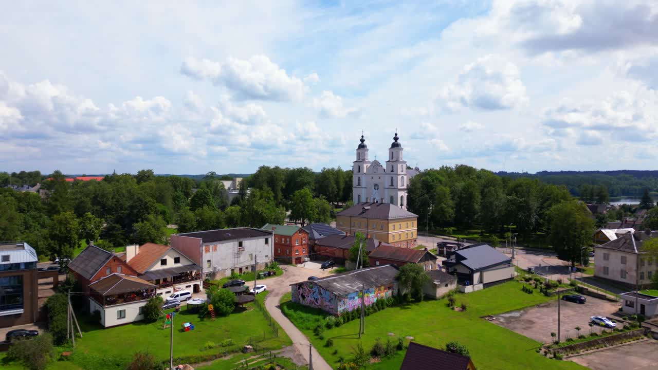 Wide aerial view of traditional homes in vibrant colors leading to the prominent church and forest edge. Shot at Zarasai, Lithuania (Zarasai, Lietuva)